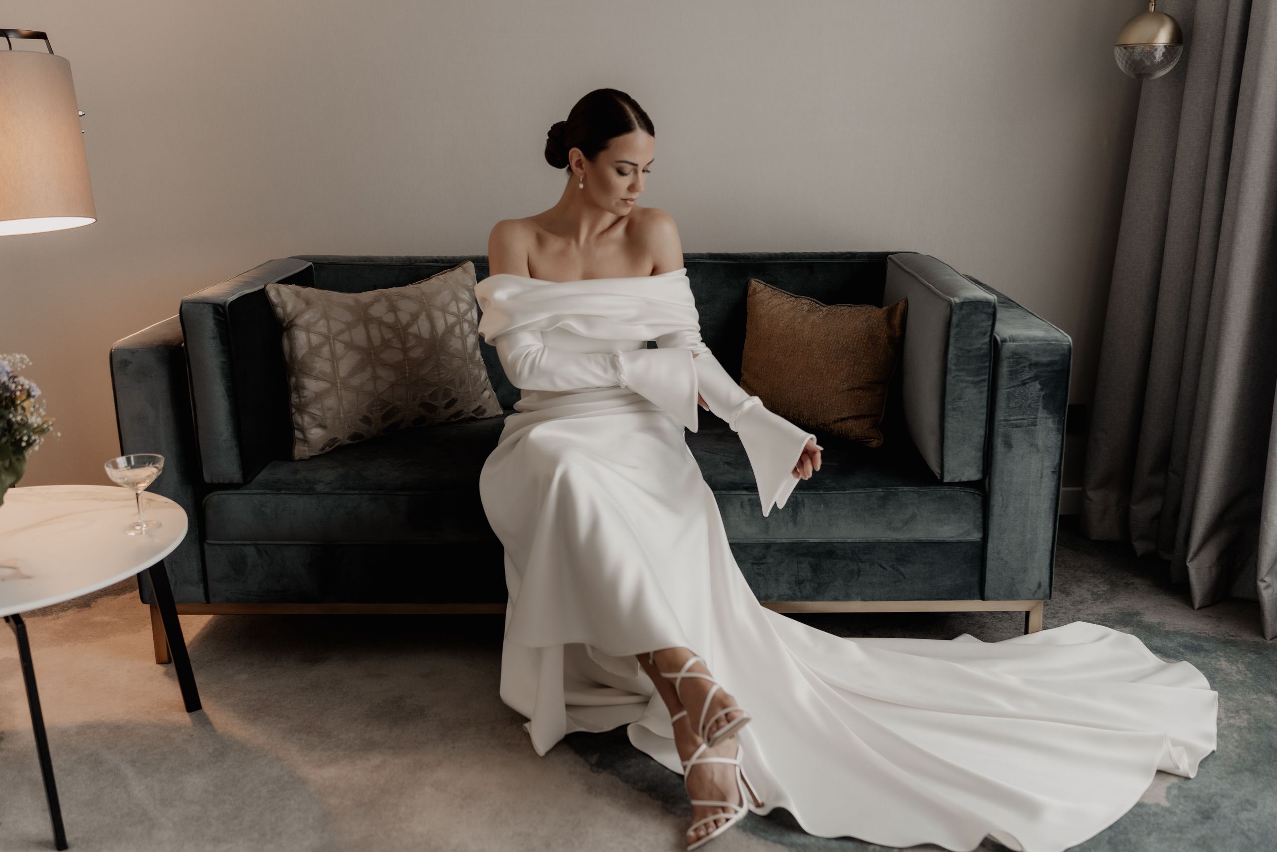 Женщина в белом платье сидит на темном диване в комнате.