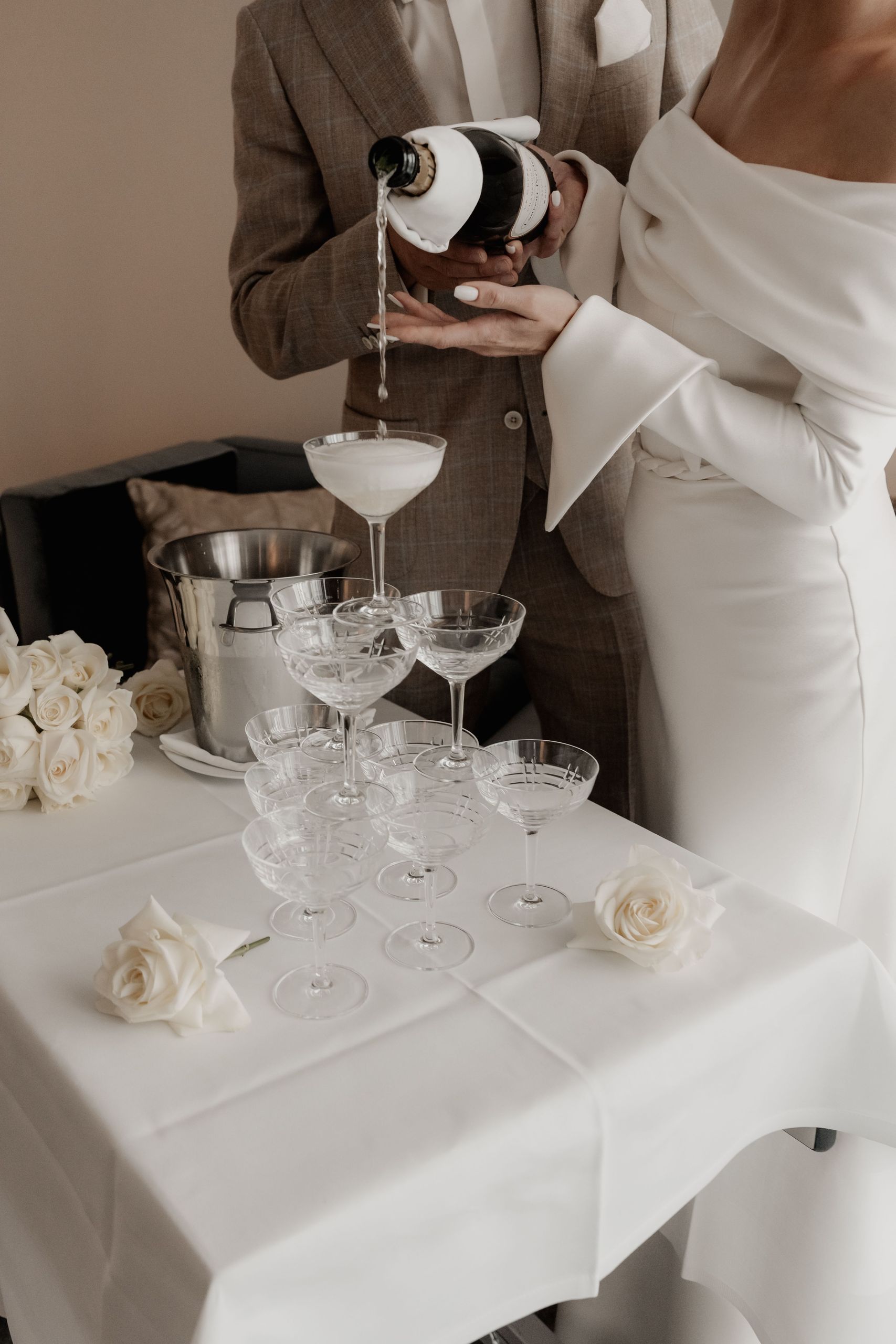 Пара наливает шампанское в пирамиду бокалов на столе, украшенном розами.