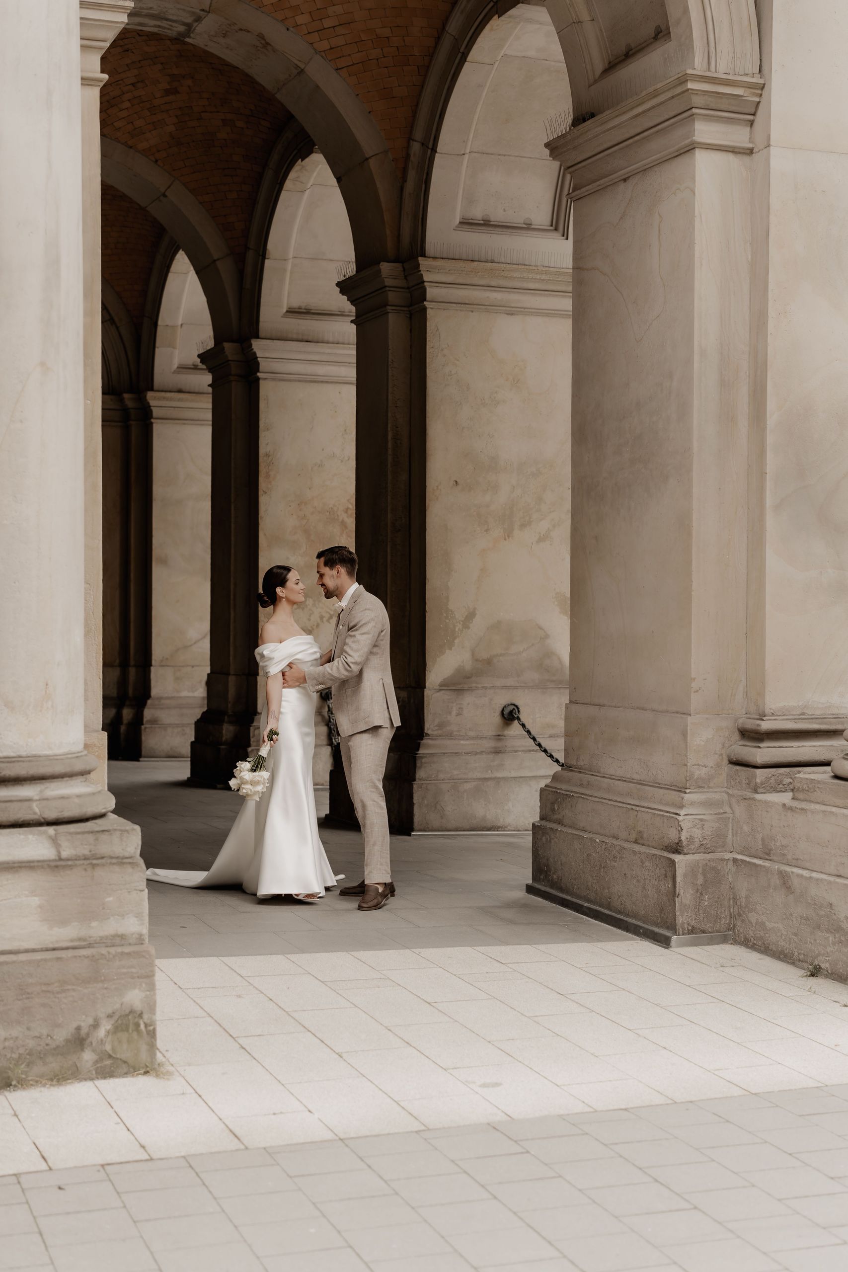 Пара в свадебной одежде стоит рядом друг с другом под каменными арками.