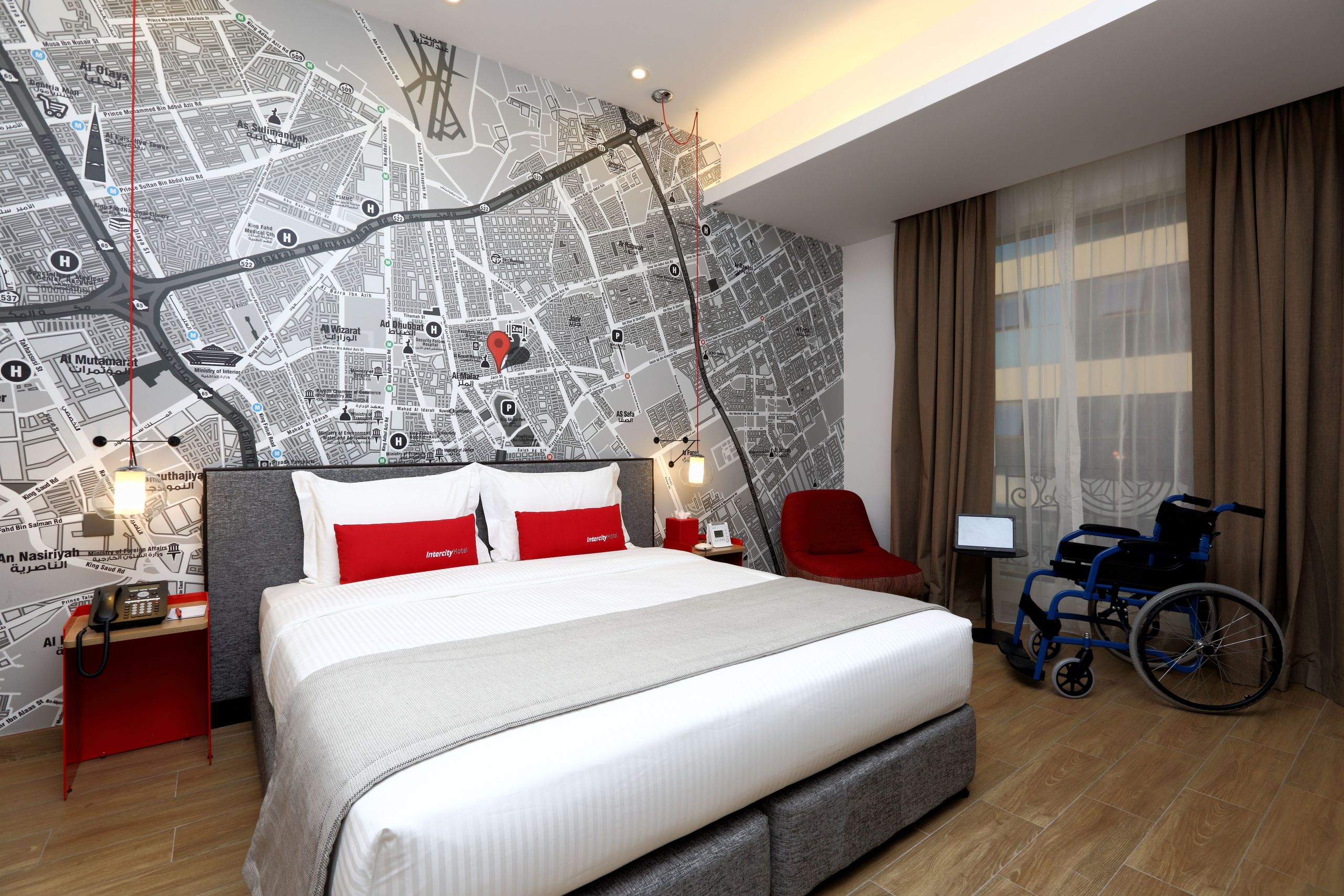 Ett modernt hotellrum med en stor säng, sängbord, en stol, en rullstol och en stor kartdesign på…