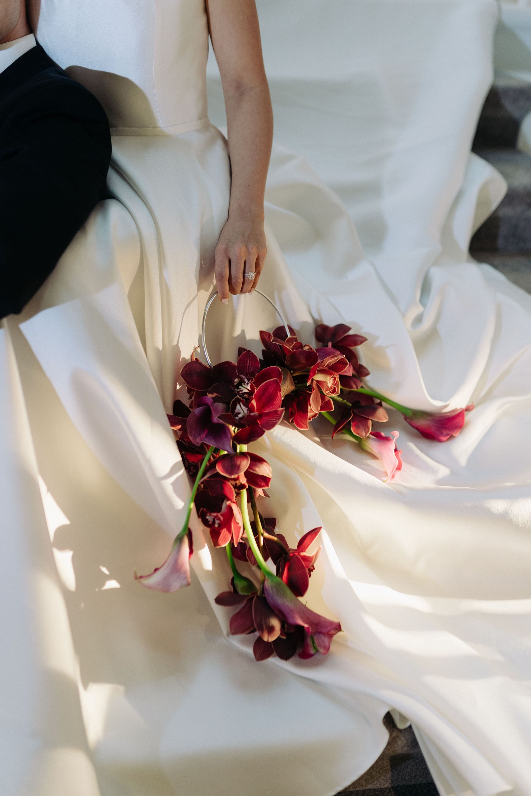 Невеста в белом свадебном платье держит букет темно-красных цветов.