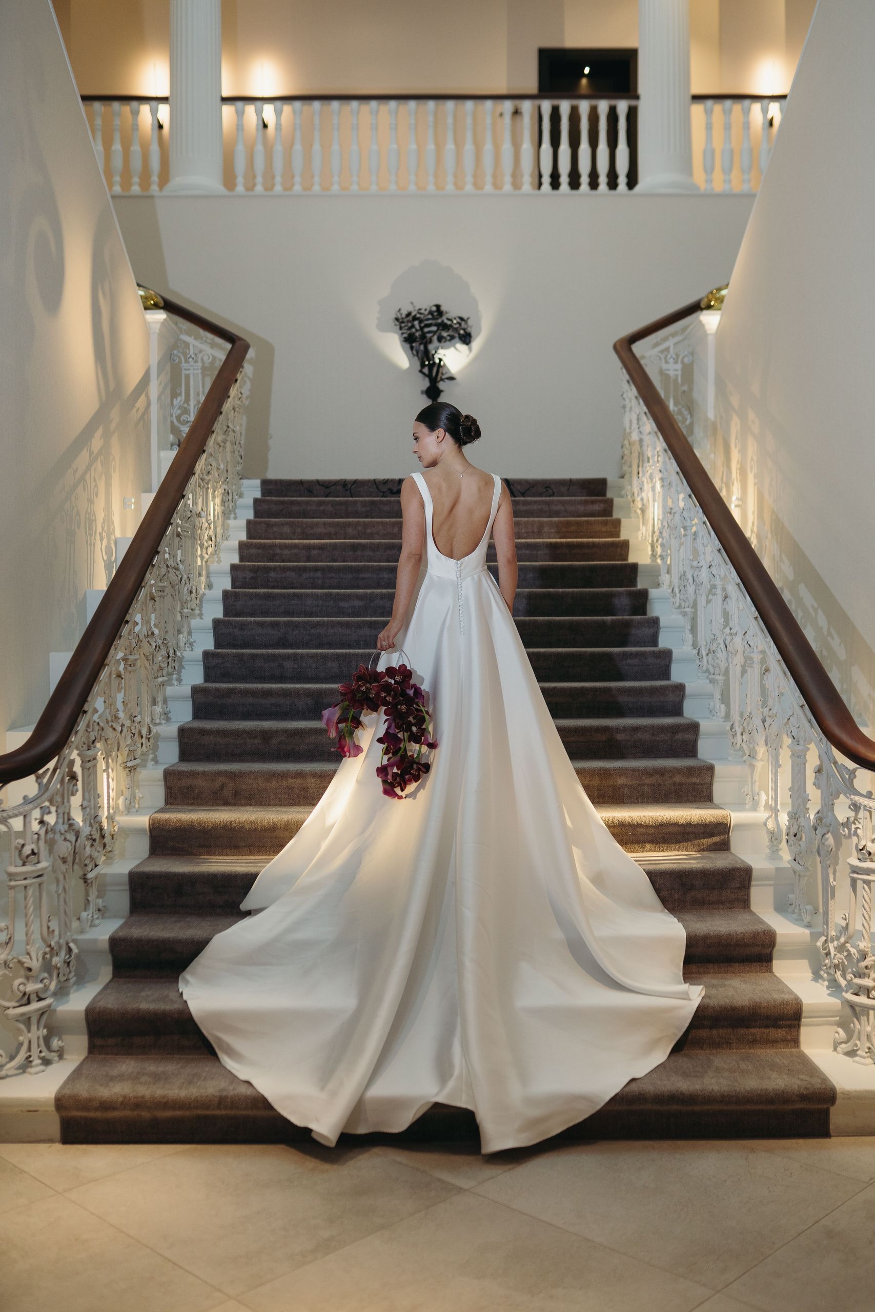 Женщина в белом свадебном платье стоит на лестнице, держа букет цветов.