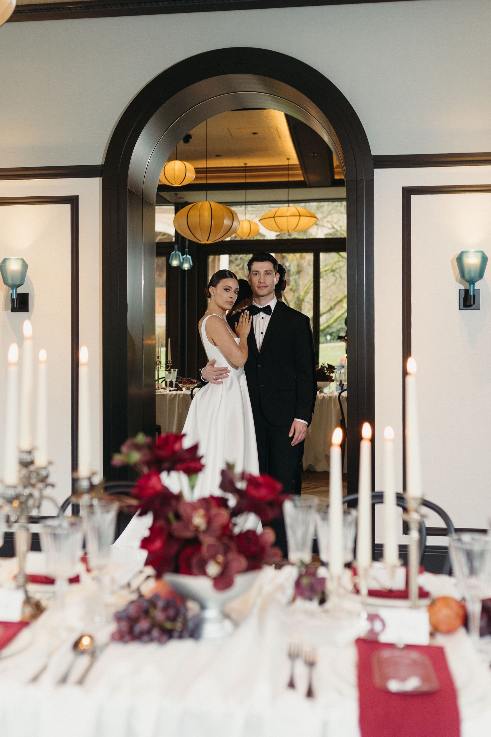 Формально одетая пара стоит в элегантной комнате, на переднем плане украшенный обеденный стол.