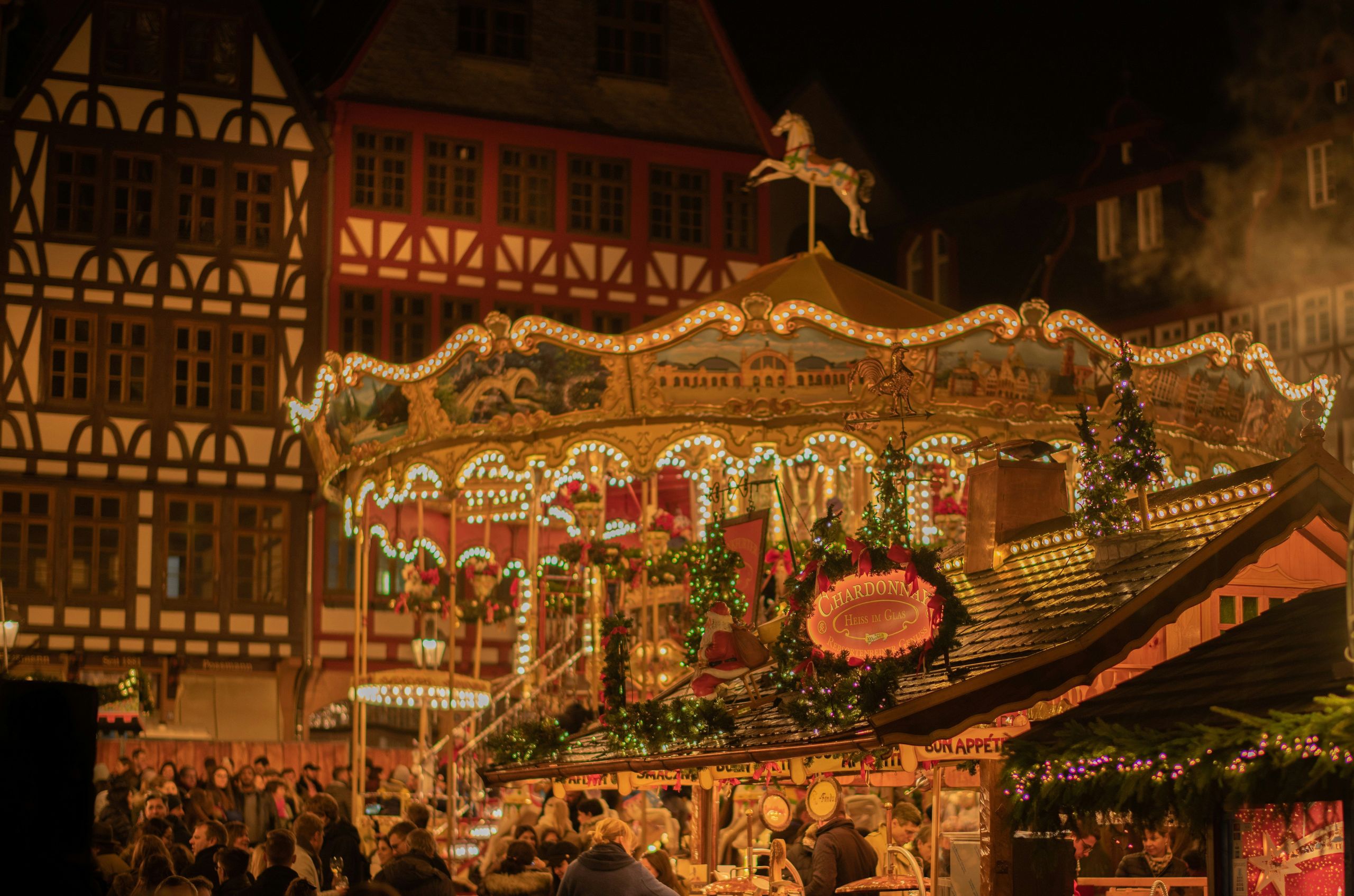 Eine festliche Nachtszene auf einem Weihnachtsmarkt mit einem Karussell und einer Menschenmenge.