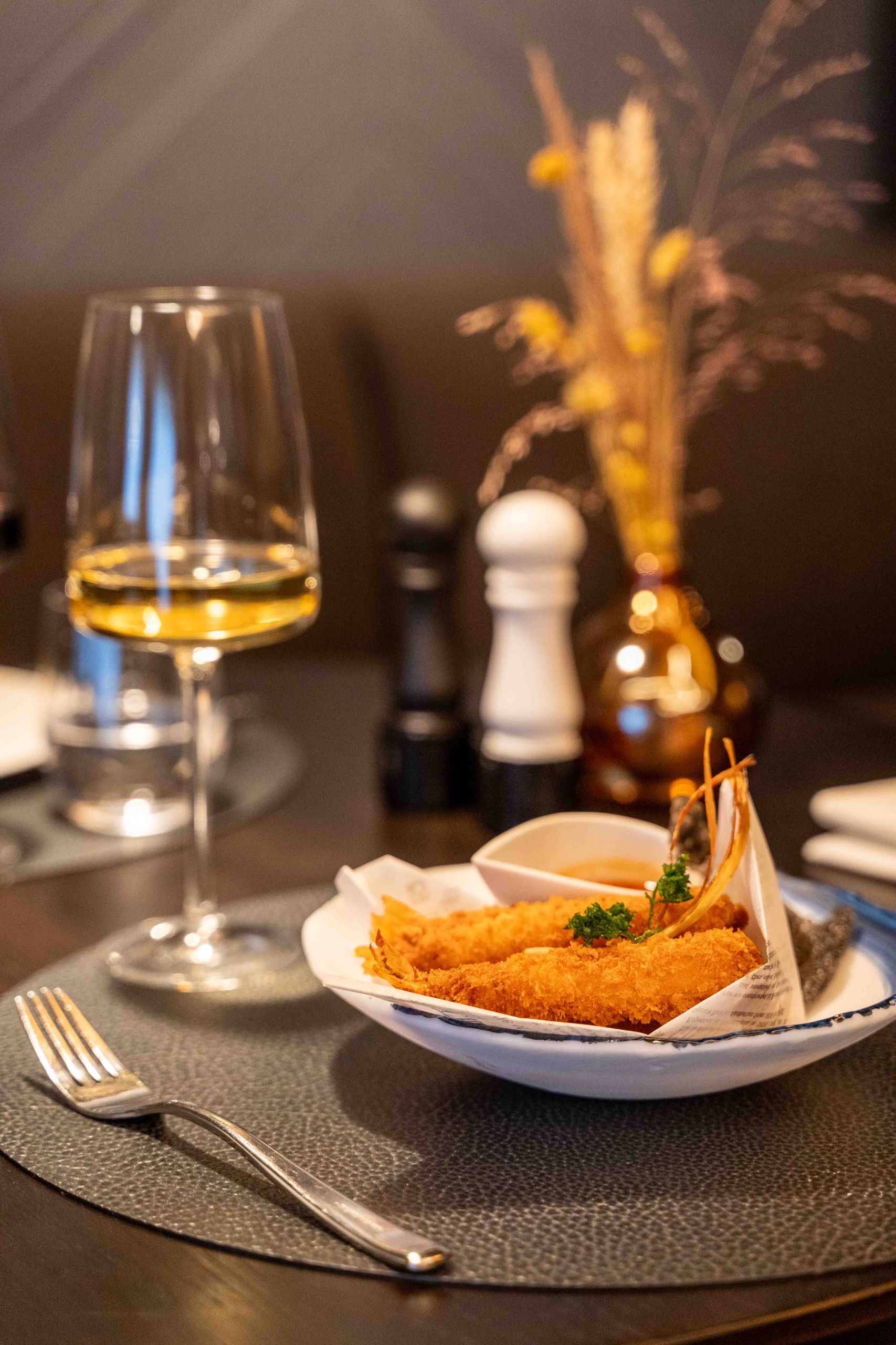 Une assiette de crevettes frites avec une sauce est posée sur une table, accompagnée d'un verre de…