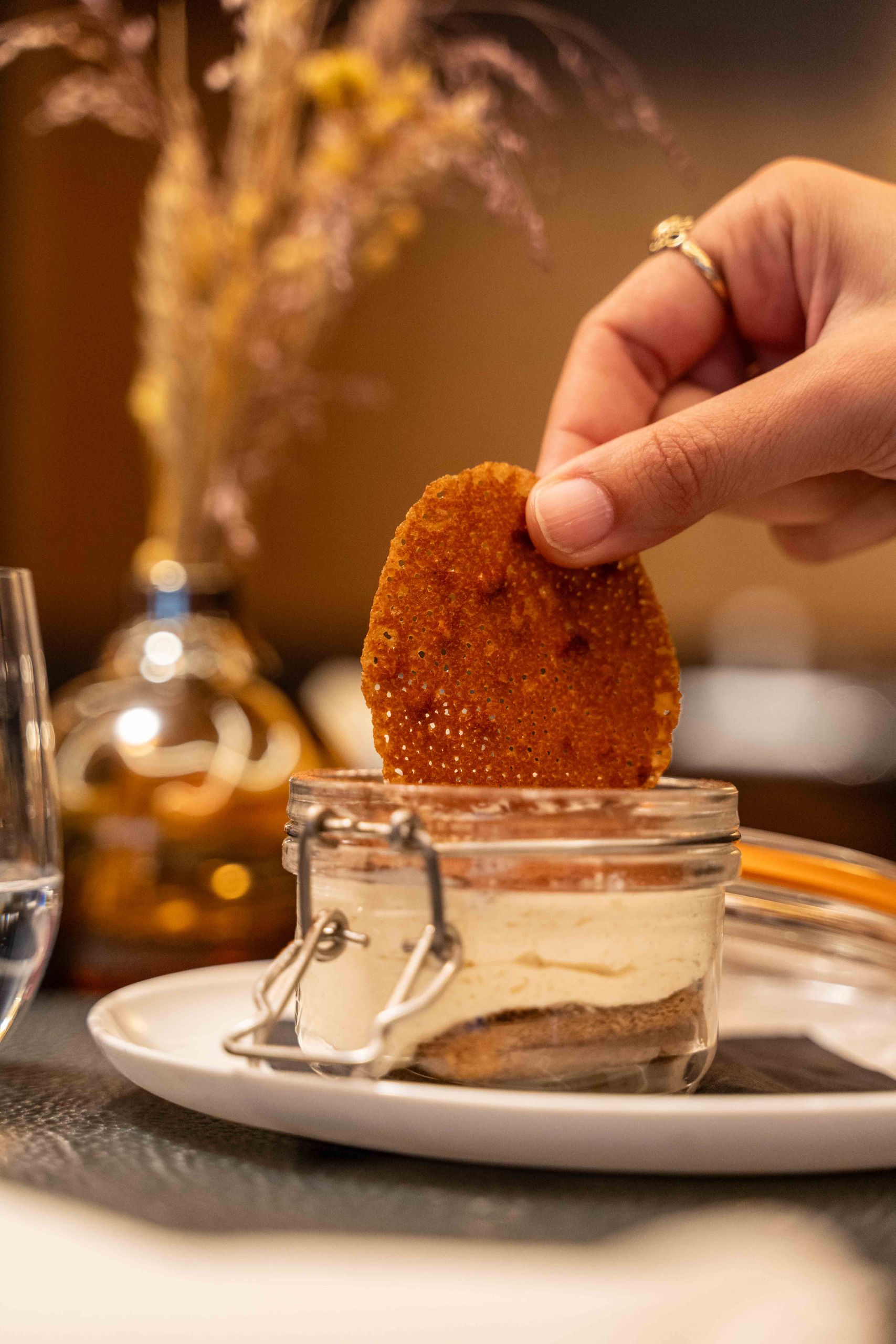 Une main trempe un biscuit dans un dessert servi dans un bocal en verre.