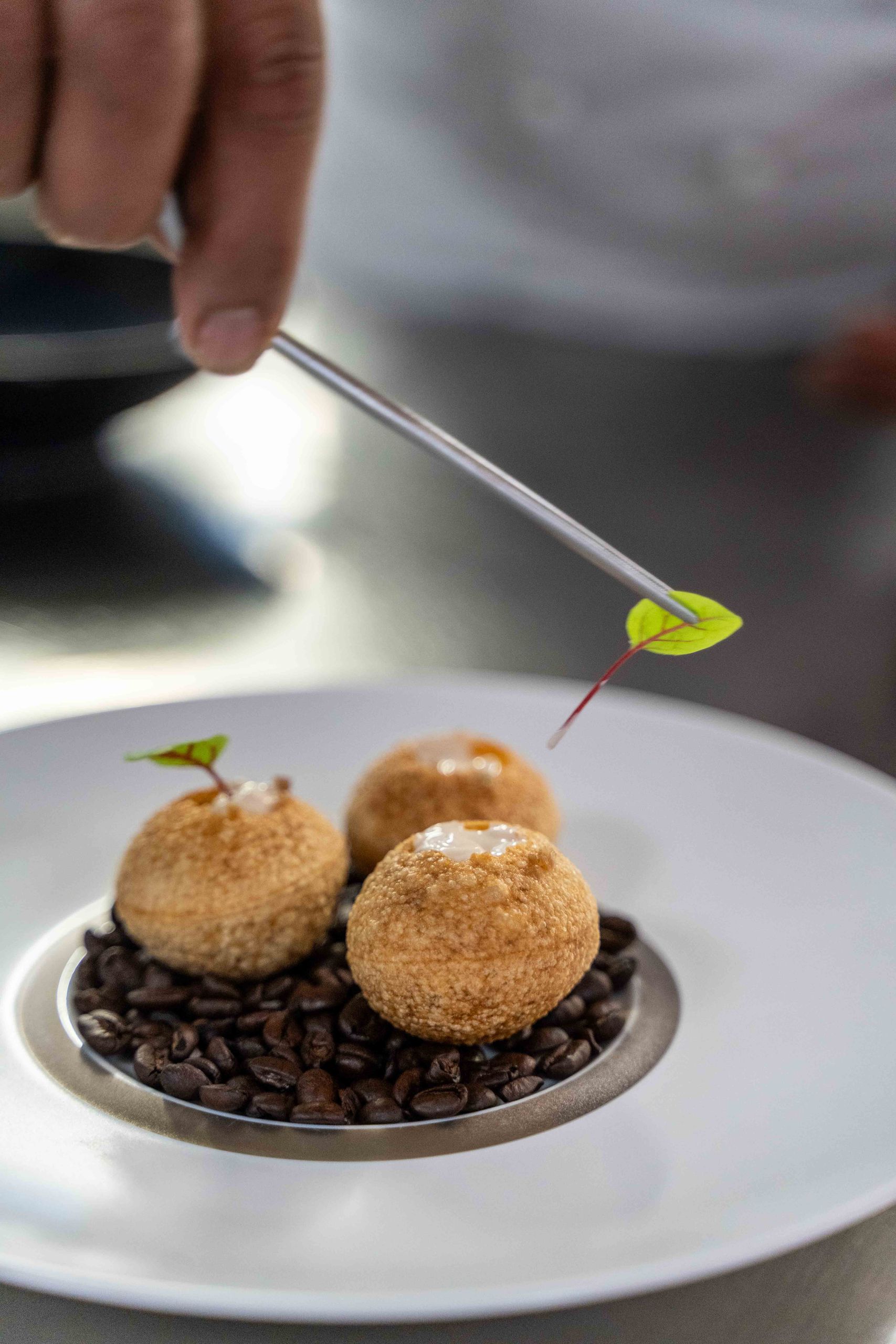 Une personne utilise une pince pour placer une petite feuille sur un dessert composé de trois…