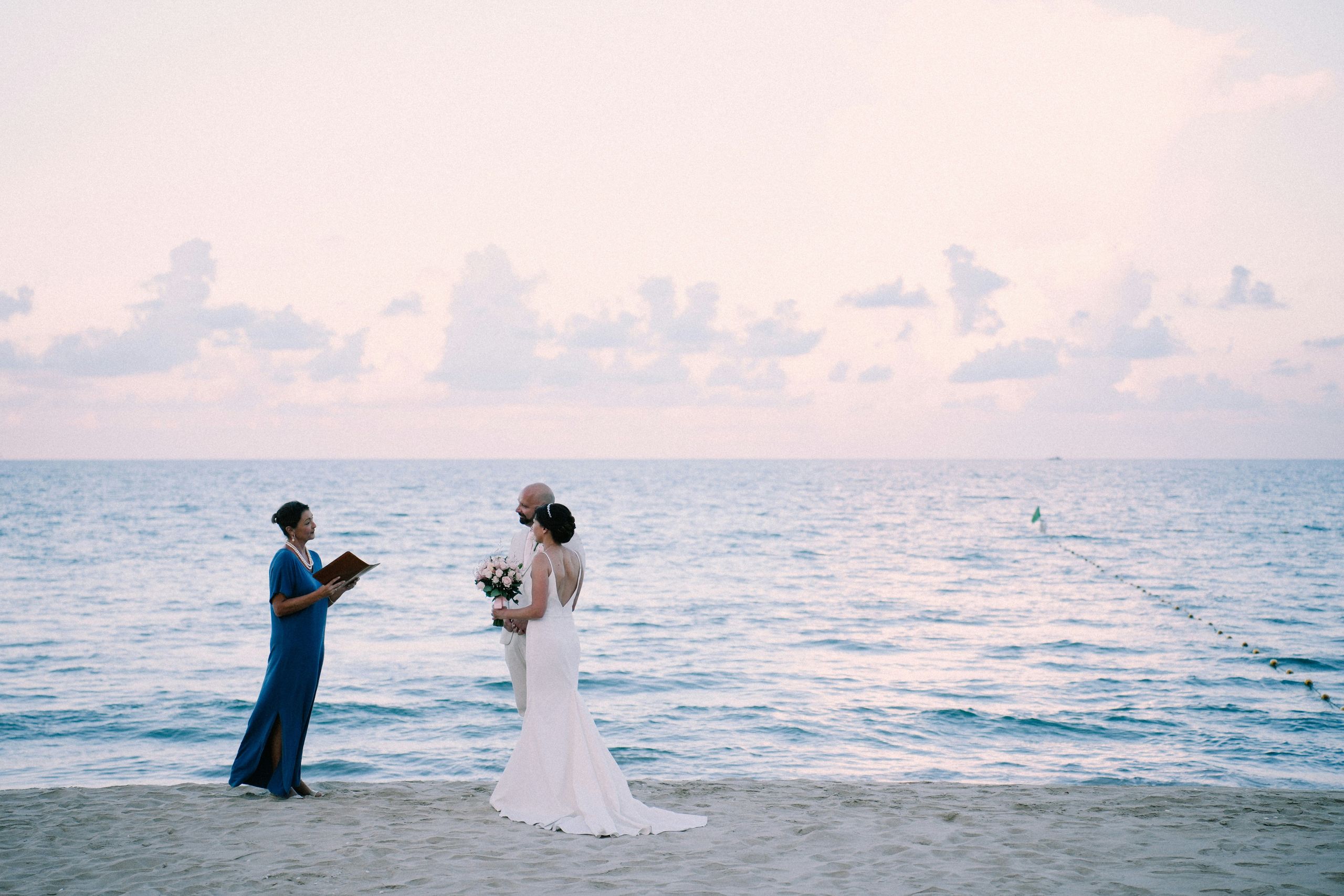 زوجان يتزوجان على الشاطئ مع وجود المأذون بجانبهما.