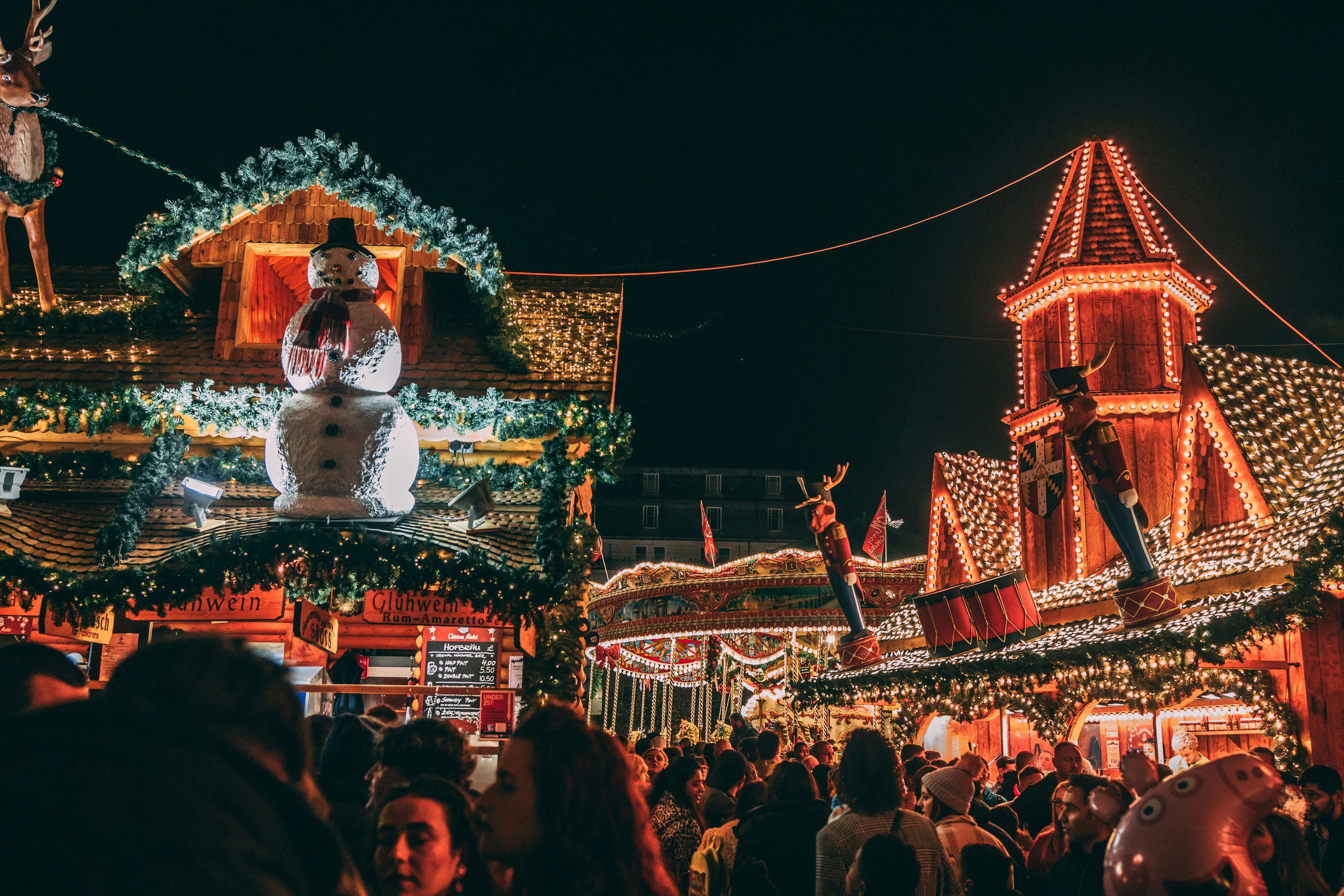 Ein überfüllter Weihnachtsmarkt bei Nacht mit festlicher Beleuchtung und Dekorationen.