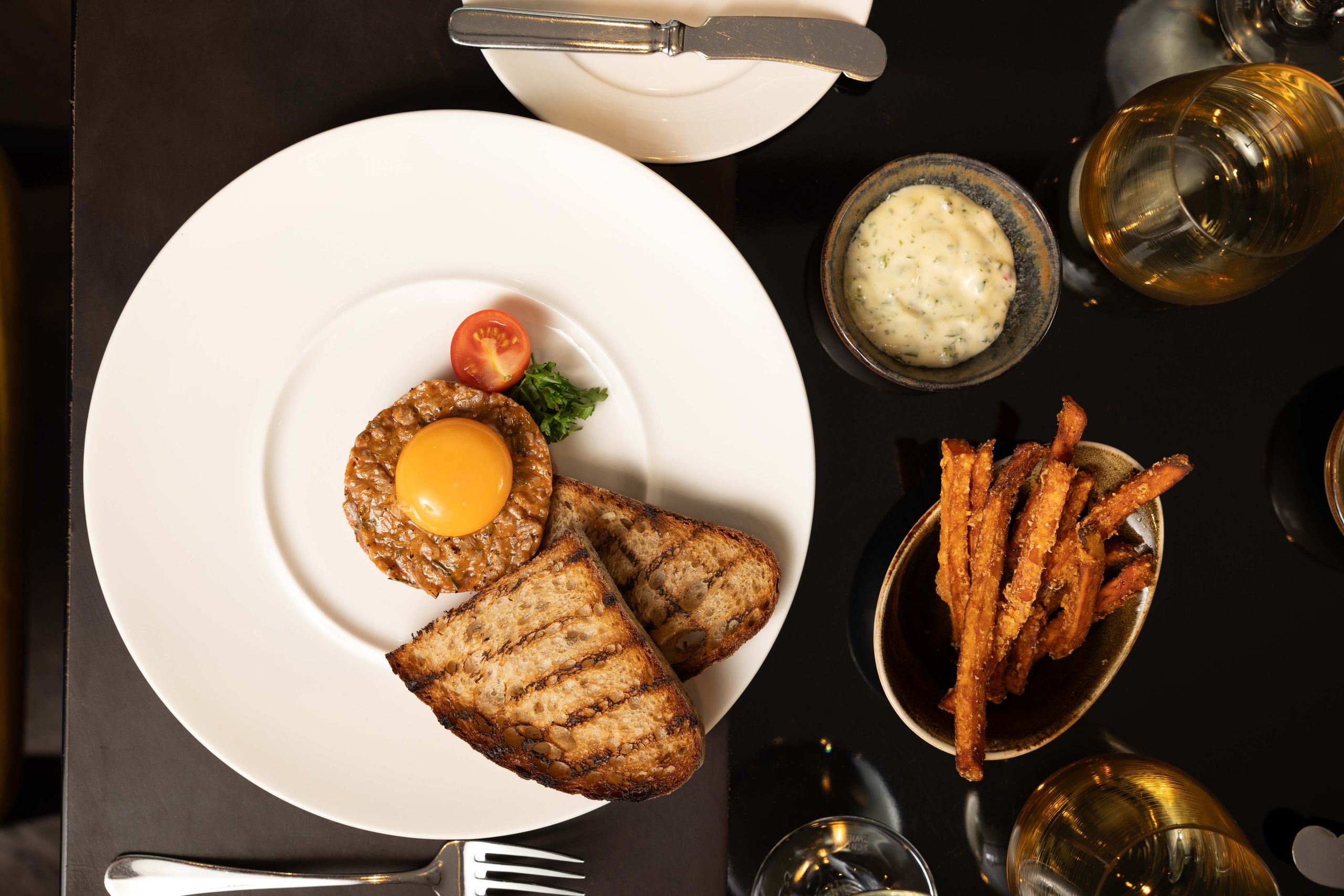 A plated meal with a cooked egg yolk on a patty, grilled bread slices, a small salad garnish, a…