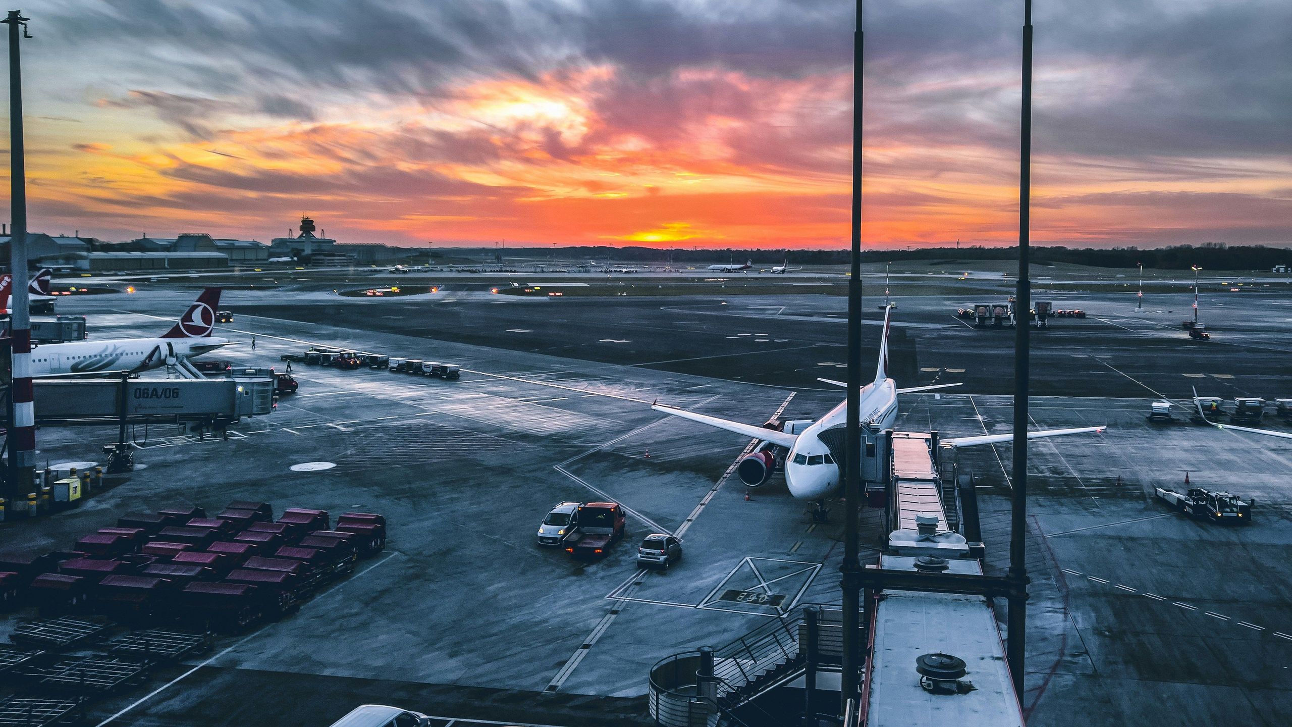 An airport runway during sunset with airplanes parked and airport vehicles nearby.