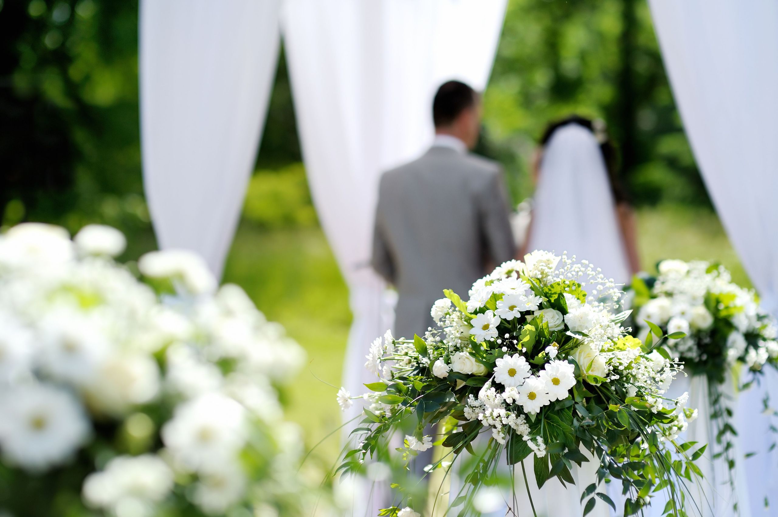 La photo montre un couple de mariés debout ensemble lors d'un mariage en plein air avec des…